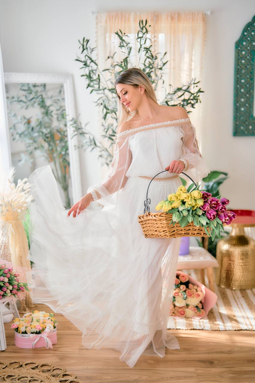 Woman in a white dress holding a basket of flowers in a decorated room.